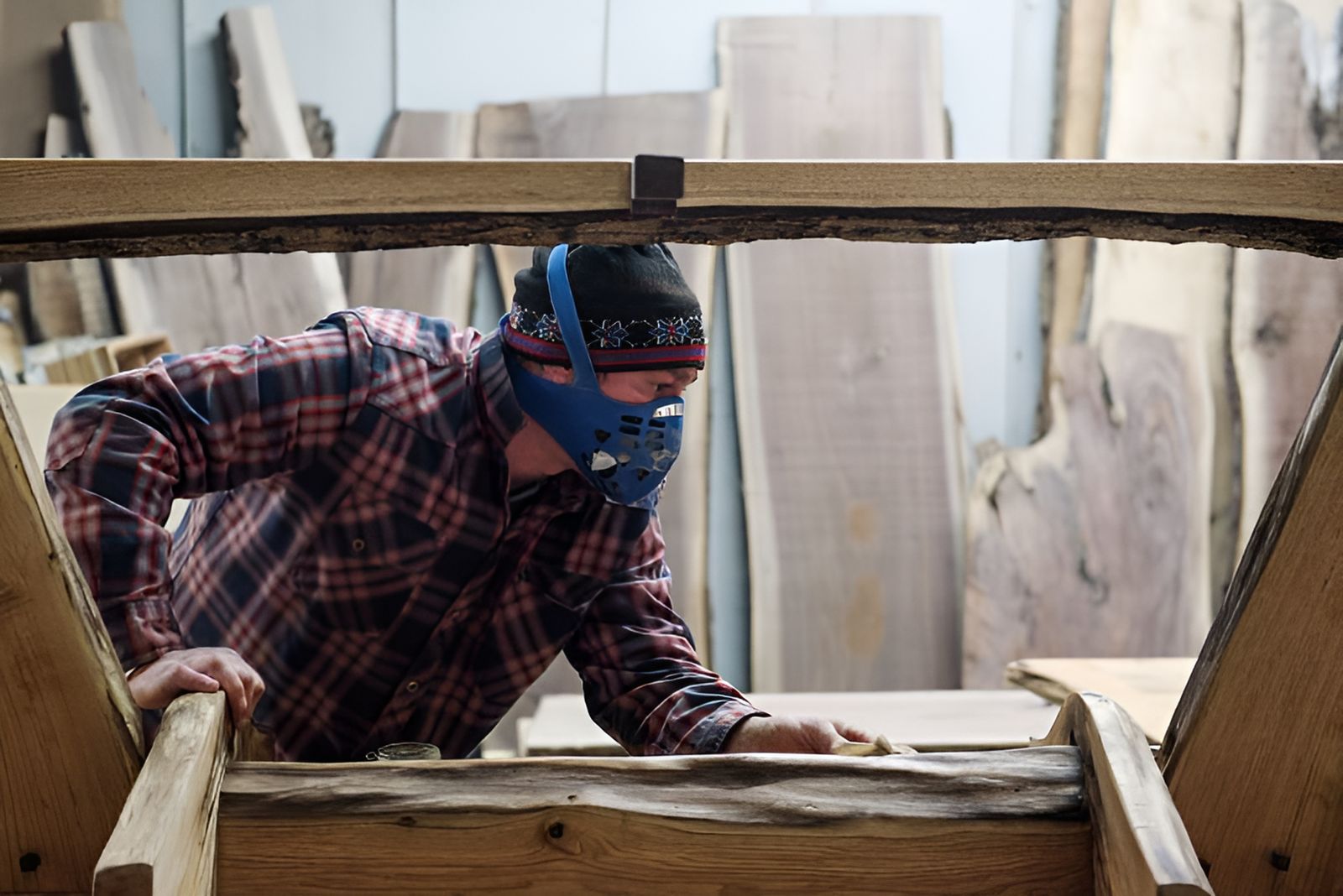 Woodworker sanding a live edge slab in front of racks of slabs